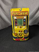 Front view of Pac-Man mini arcade game in original yellow packaging showing game screen and controls.