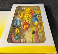 Photo of boxed Simpsons Movie collectible figures showing all six characters through clear window in original white and yellow packaging.