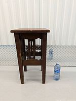 Front view of small wooden side table next to water bottle for scale showing rectangular top and vertical side slats.