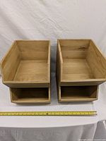 Two wooden storage boxes showing angled sides and lower open shelf compartments, placed on table with measuring tape indicating approximate length of 16 inches.
