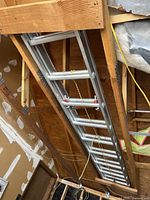Photo showing an aluminum extension ladder stored in a garage ceiling area, hanging horizontally with visible rungs and locking mechanisms.