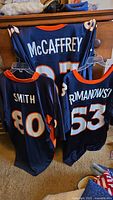 Photo showing all three Broncos jerseys with player names and numbers visible: McCaffrey #87, Smith #80, Romanowski #53.