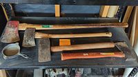 Four axes laid out on a black shelf, including a large 36" Forest King wood chopper axe and three smaller axes or hatchets, showing wooden handles and metal heads with signs of wear.