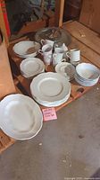 Wide view of entire ceramic dish set including stacked plates, bowls, cups and service platters arranged on wooden surface.