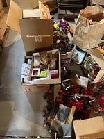 Boxed assortment of string lights, ornaments and floral pieces on concrete floor