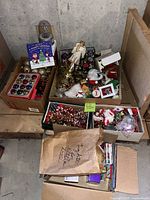 Overview of cardboard boxes containing assorted Christmas ornaments, tinsel picks, plush figures and a book