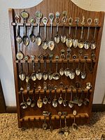 Full front view of a wooden spoon display rack fully loaded with a variety of collectible spoons with detailed thematic handles.