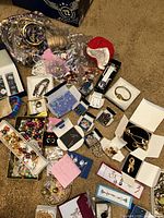 Various pieces of Avon costume jewelry spread on the floor including pins, bracelets, earrings, lockets, and bead strands, some in Avon boxes and bags.