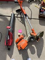 Overview of the weed trimmer/edger, leaf blower, hand clippers, and cord all together on concrete surface.
