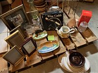 Photo of assortment arranged on wooden platform showing frames, wine caddy boxed set, dishes, teapot flower holder, glasses, and ceramic pieces.