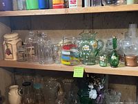 Wide view of glass pitchers, drinking glasses, and storage containers on wall shelves showing multiple glassware pieces including colorful and floral decorated pitchers and various clear glasses.