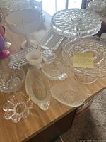 Wide view showing multiple crystal and glass kitchen serving items on a wooden surface, including cake plates and assorted dishes.