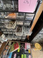 Close-up of a small plastic drawer unit with screws, nails, bolts, and fasteners, along with boxes of staples and other materials below.