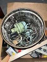 Top-down photo showing a metal container holding several green electrical/mechanical parts, wires, and clamps, with additional miscellaneous items surrounding it.