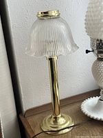 Brass hurricane lamp with ribbed glass shade on wooden table