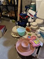 Photo showing multiple plastic containers with lids, a pink decorative item, blue bowl, and stacked containers on a basement floor.