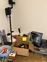 Photo showing miscellaneous items including metal detector, remote control boat and car, electronic game box, poker chips box and playing cards box arranged on floor