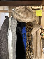 Various ladies coats and accessories including beige faux fur coat with matching hat, and multiple coats in different fabrics and colors hanging on a rail.