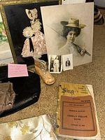Photo showing vintage artwork, a decorative baby shoe, a couple of small photographs, a textured black clutch, a German phrase book from 1943, and a note indicating mixed vintage gloves and accessories