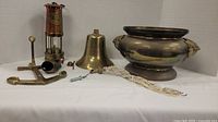 Photo showing the complete lot including the large brass bowl with figure handles, brass bell with rope, and antique mining lamp.