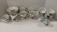 View of 4 Evesham mugs, cream and sugar set, 2 egg coddlers, 5 ramekins and 6 small bowls all in white china with fruit designs and gold rims.