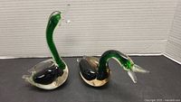Two green glass swans side by side, different neck positions and sizes.