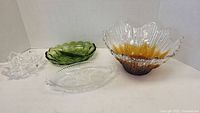 Four glass bowls shown on white backdrop: large orange-tinted bowl, green olive dish, clear oval dish, and clear decorative bowl.