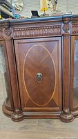 Front view of central wood cabinet door showing carved detailing, oval veneered panel, and lion head ring pull.