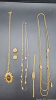 Full lot including a large pendant necklace with tiger's eye, seed pearl necklace and bracelet, multi-pearl necklace, and earrings on black background.