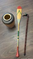 Photo of all three items: tall striped ceramic pot, painted wooden canoe paddle, and a walking cane with carved duck head handle