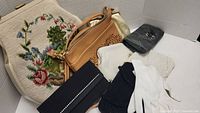 Lot includes vintage needlepoint purse with detailed floral and scenic embroidery, tan leather purse with floral laser cut pattern, beaded purses in black and white, and white ladies gloves.
