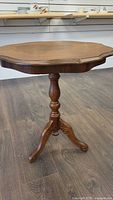 Side view of the wooden side table showing the turned pedestal leg and tripod base with carved scroll details.