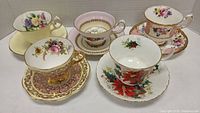 Overview of 5 floral teacups and saucers with various pink, cream backgrounds and gold trim