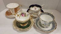 Four distinct bone china teacups with matching saucers displayed showing detailed patterns and gold accents.
