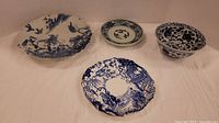 Four blue and white vintage dishes including large plate, small dish, square plate, and bowl.