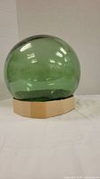 Single green vintage glass fishing float resting on cardboard base against a white draped background.
