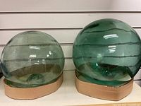 Two large light green tinted vintage glass fishing net floats on cardboard ring bases, displayed against a white panel background.