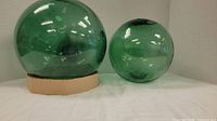 Pair of two green glass fishing net floats, larger and smaller, showing spherical shape, color, and condition