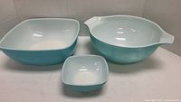 Three blue vintage Pyrex mixing bowls displayed side by side showing size variations and shape differences