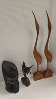 Photo showing all four wood carved figures together: two tall wooden bird sculptures, one sailfish figure, and one bust statue.