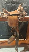 Left side view of leather Western saddle showing fenders, stirrups and latigo ties