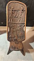 front view showing carved figurative panels, seat, and dark stain