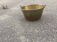 Side view of brass cauldron with iron handle on pavement