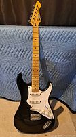 Full front view of black Aria Pro II Fullerton Strat-style guitar standing upright
