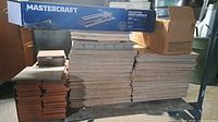 Stack of various sized tiles with boxed Mastercraft tile cutter and cardboard box