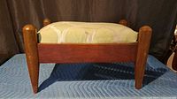 Side view of wood ottoman showing tapered legs and upholstered cushion