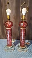 Both matching cranberry cut glass table lamps standing upright with bulbs attached