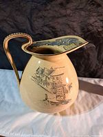Side view of cream ceramic pitcher showing village scene decoration