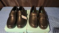 Two pairs of black slip-on loafers on top of Apex boxes