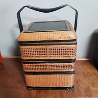 Front view of the antique Chinese 3-tiered woven storage basket with black lacquered wooden handle and top.
